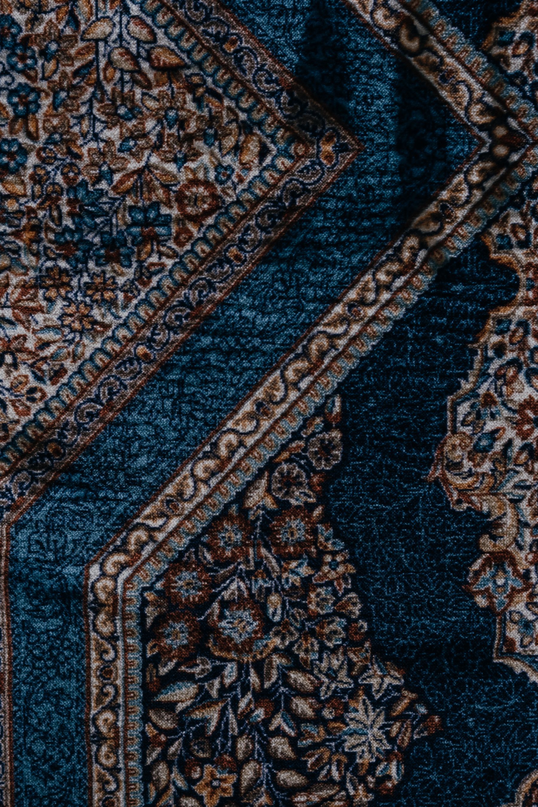 Close detail of a hand-knotted rug: indigo field, madder-red and camel border motifs, individual wool knots visible.